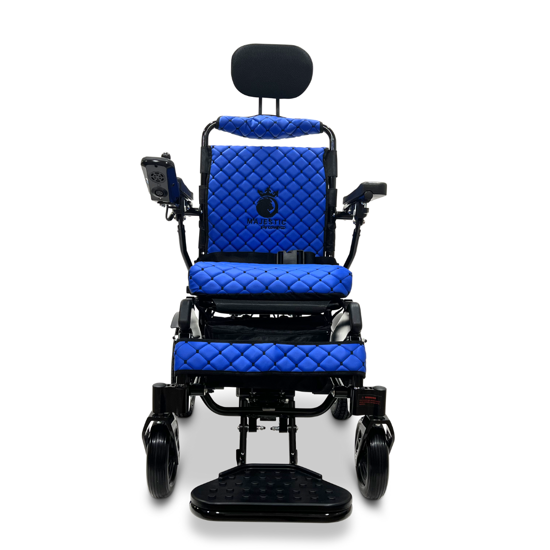 The image showcases a front view of the ComfyGo MAJESTIC IQ-9000 Auto Recline Remote Controlled Electric Wheelchair, featuring a blue quilted seat, backrest, and armrests. It includes a headrest and a digital joystick controller on the right armrest for improved maneuverability. The wheelchair is equipped with brushless silent motors and footrests, set against a plain white background.