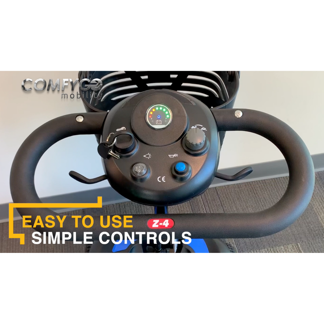 Close-up of the ComfyGo Z-4 Ultra-Light Electric Mobility Scooter handlebar showing a control panel with speed dial, battery indicator, and key slot. COMFYGO mobility and EASY TO USE SIMPLE CONTROLS text are visible. The scooter rests on carpeted flooring.