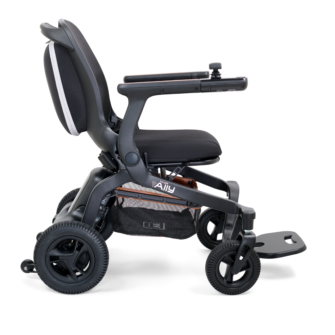 Side view of the black Golden Tech Ally Folding Power Wheelchair, featuring a cushioned seat and backrest, armrests, a joystick on one armrest, four wheels, and a foldable footplate. This sleek wheelchair is mobile app-controlled and perfect for travel.