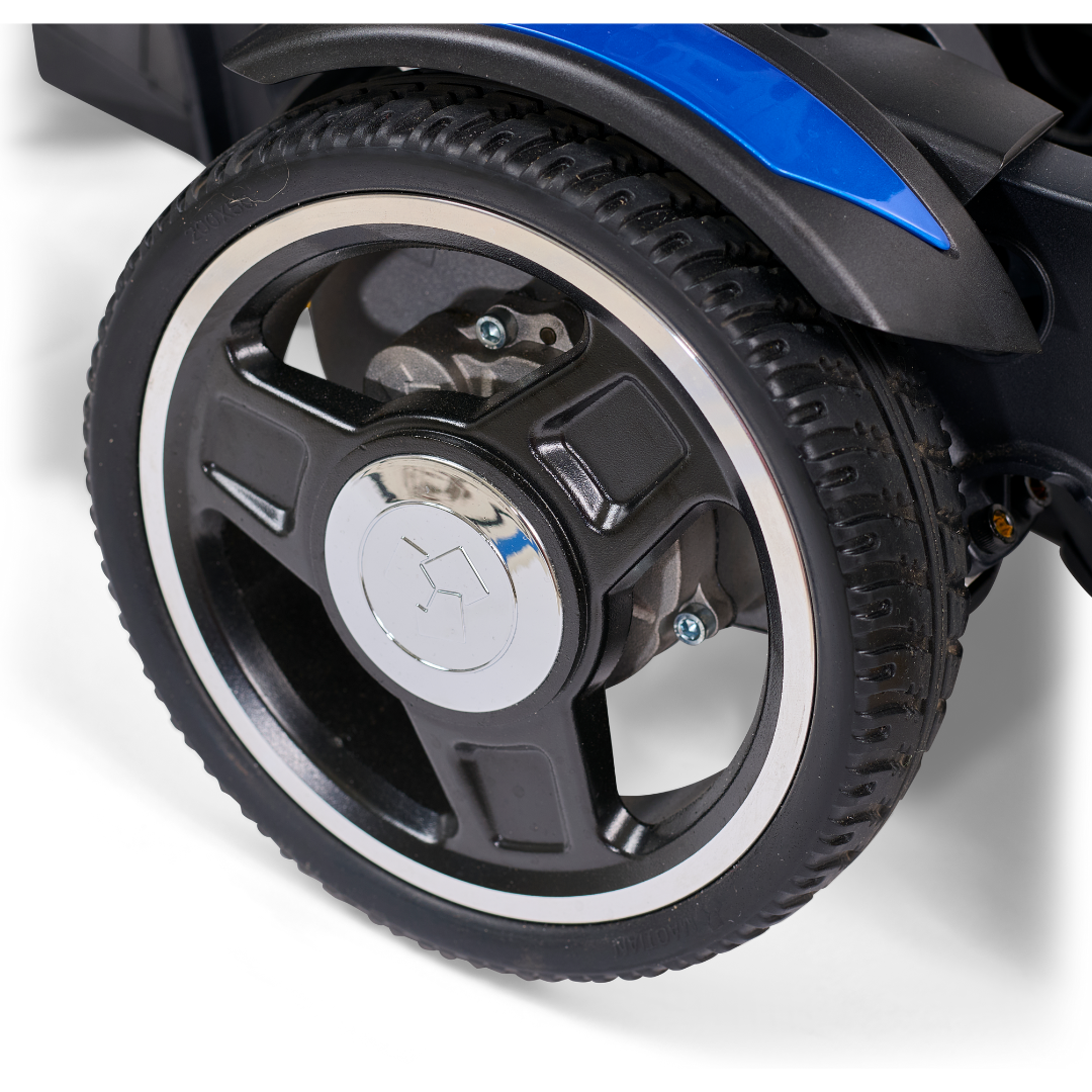 Close-up of a five-spoke black wheel with a silver hub on the Golden Tech GP130 Buzzaround CarryOn Portable Powerchair. The surrounding parts feature black and blue colors. The tires tread pattern is clear, suggesting its new or barely used.