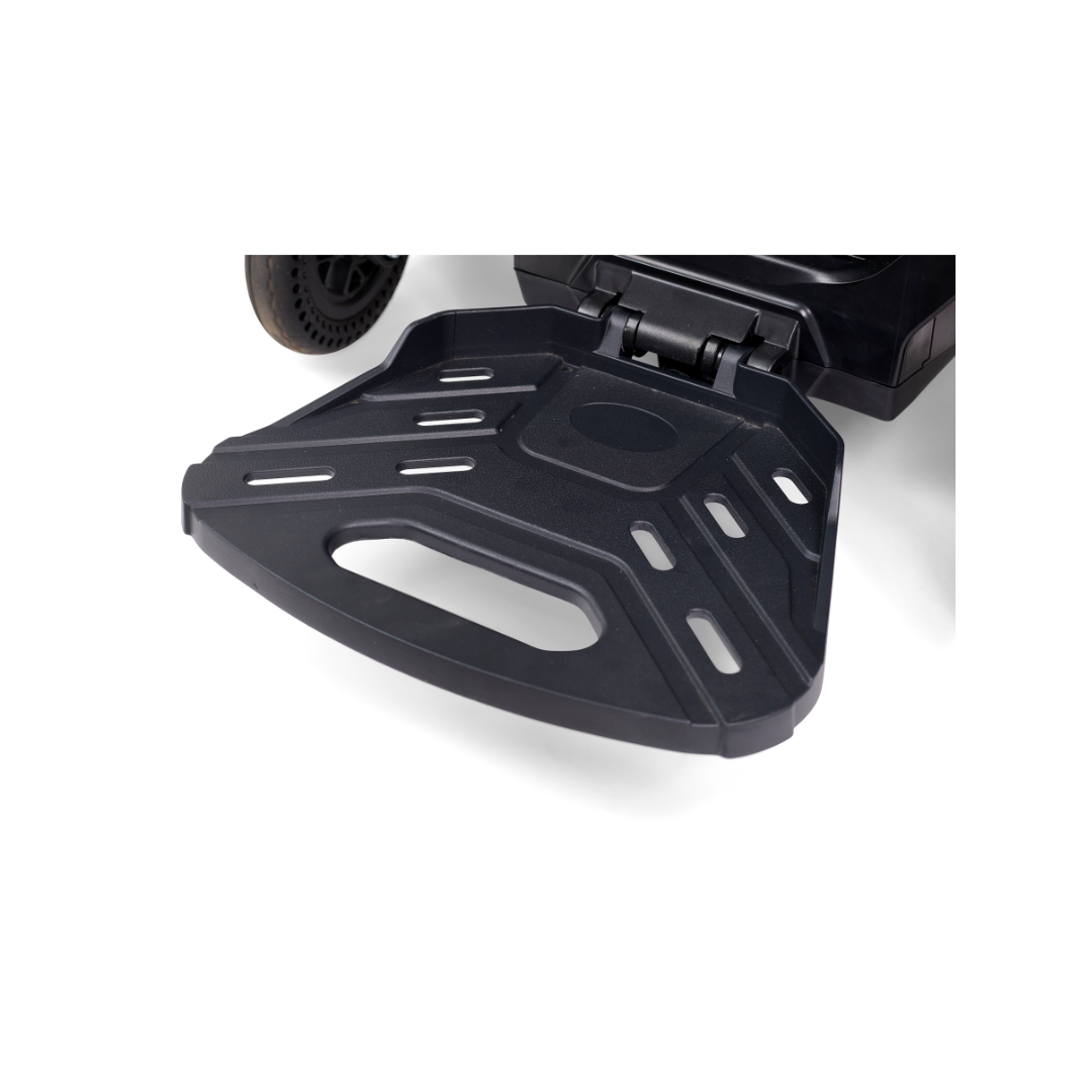 Close-up of the ultra-compact, foldable footplate on the Golden Tech GP130 Buzzaround CarryOn Portable Powerchair. The black footplate has a textured surface, slots, and a handle cutout for easy folding, complementing the scooters 4-wheel suspension for enhanced stability.