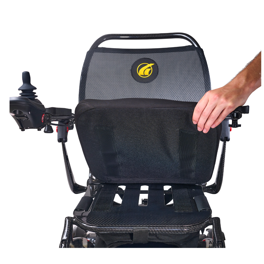 A person lifts the seat cushion of the Golden Tech Carbon Fiber Cricket Power Wheelchair, which weighs only 33 lbs and features a mesh backrest plus a joystick control on the left armrest.