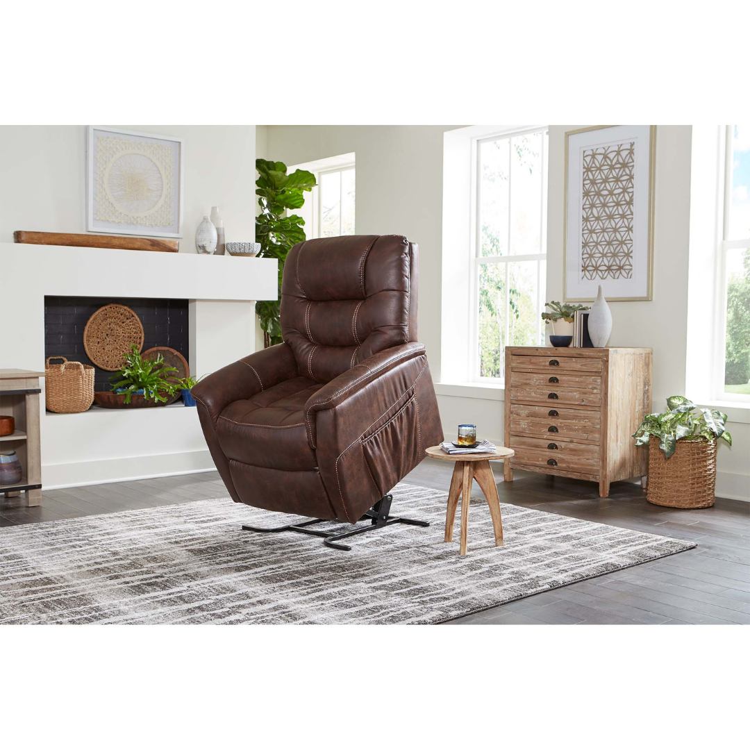 The Golden Tech PR446 DeLuna™ Dione Recliner with Lift Assist in brown faux leather is partially lifted in a bright living room featuring large windows, a striped rug, wooden side table, greenery, and modern decor.