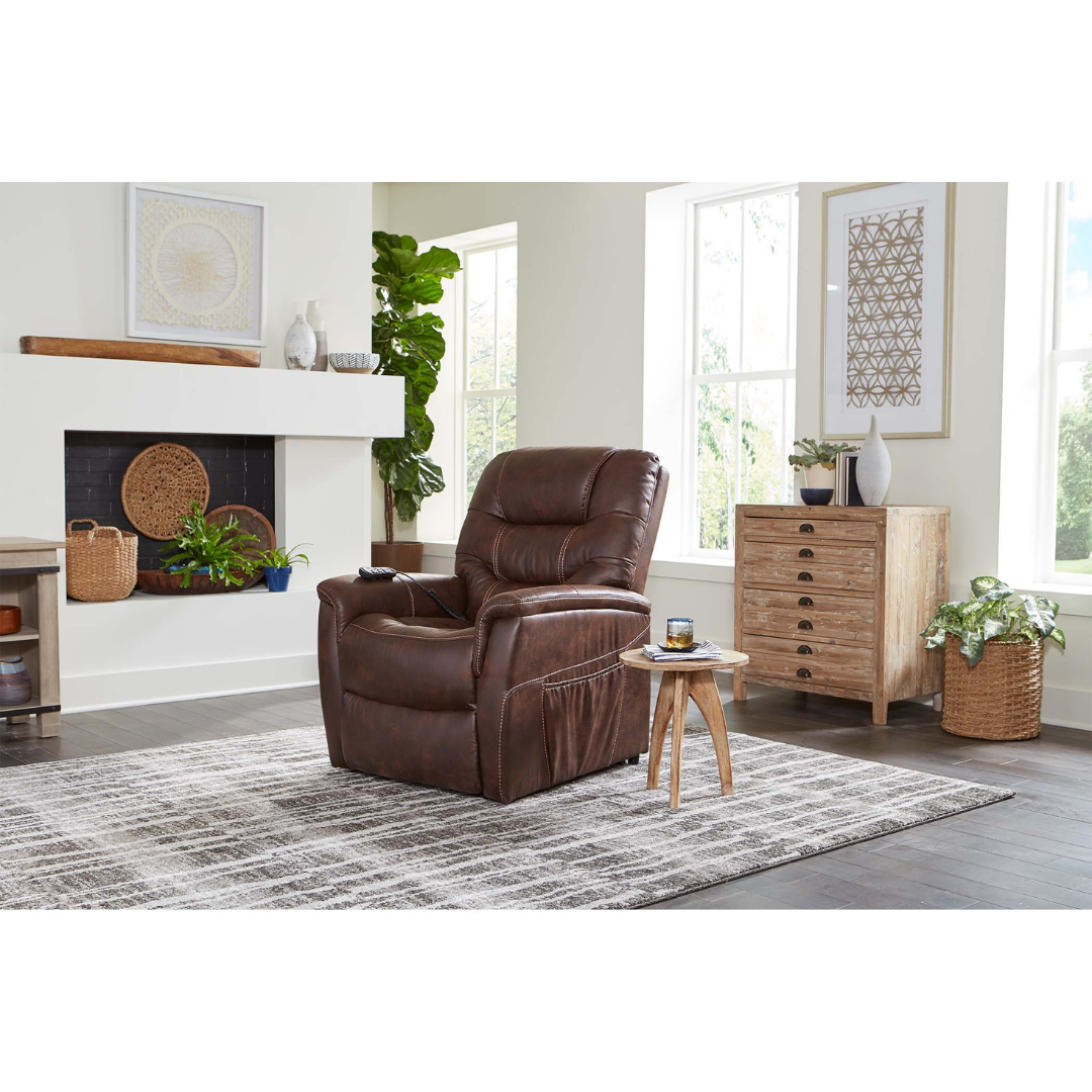 The Golden Tech PR446 DeLuna™ Dione Recliner with Lift Assist, in brown faux leather, sits on a gray patterned rug in a bright living room with white walls, large windows, plants, and light wood furniture.