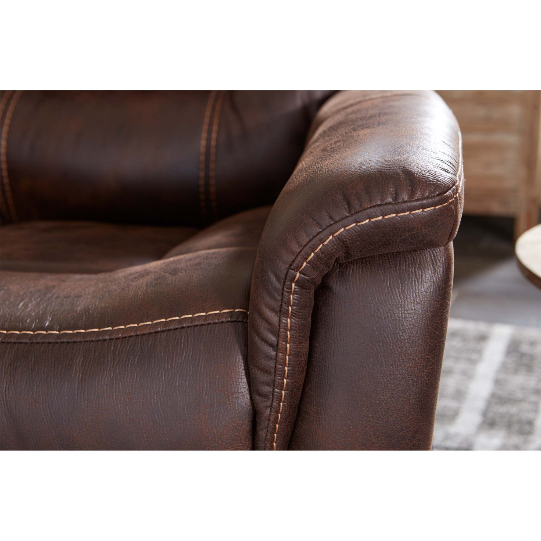 Close-up of the Golden Tech PR446 DeLuna™ Dione Recliner with Lift Assist in brown faux leather, featuring visible stitching and textured surface; armrest and seat shown with a patterned rug and wood furniture in the background.