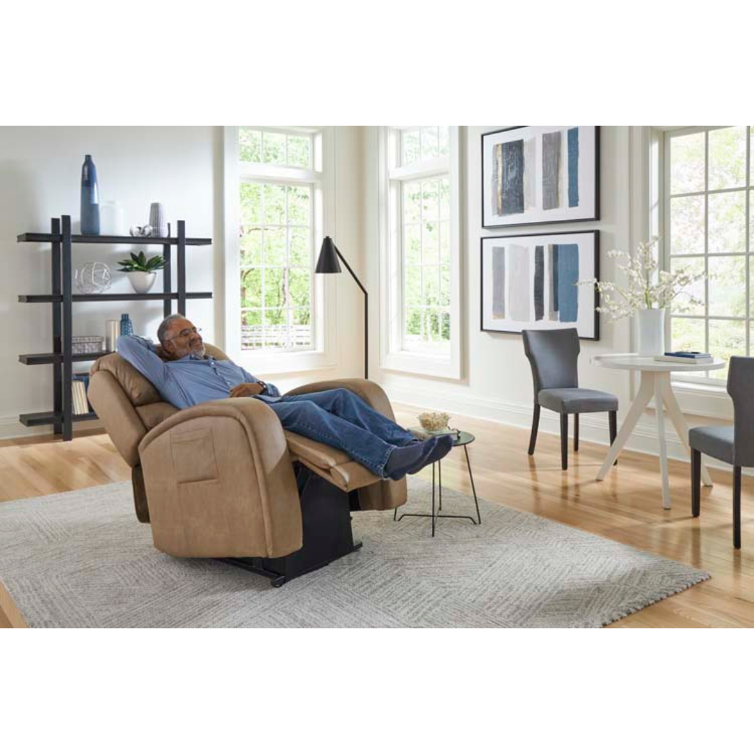 In a bright living room adorned with abstract art, a small round table with chairs, and a black bookshelf, someone relaxes in the Golden Tech PR761 EZ Sleeper Recliner with Lift Assist & Twilight Recline. Nearby, a floor lamp stands on a light-colored rug by large windows.