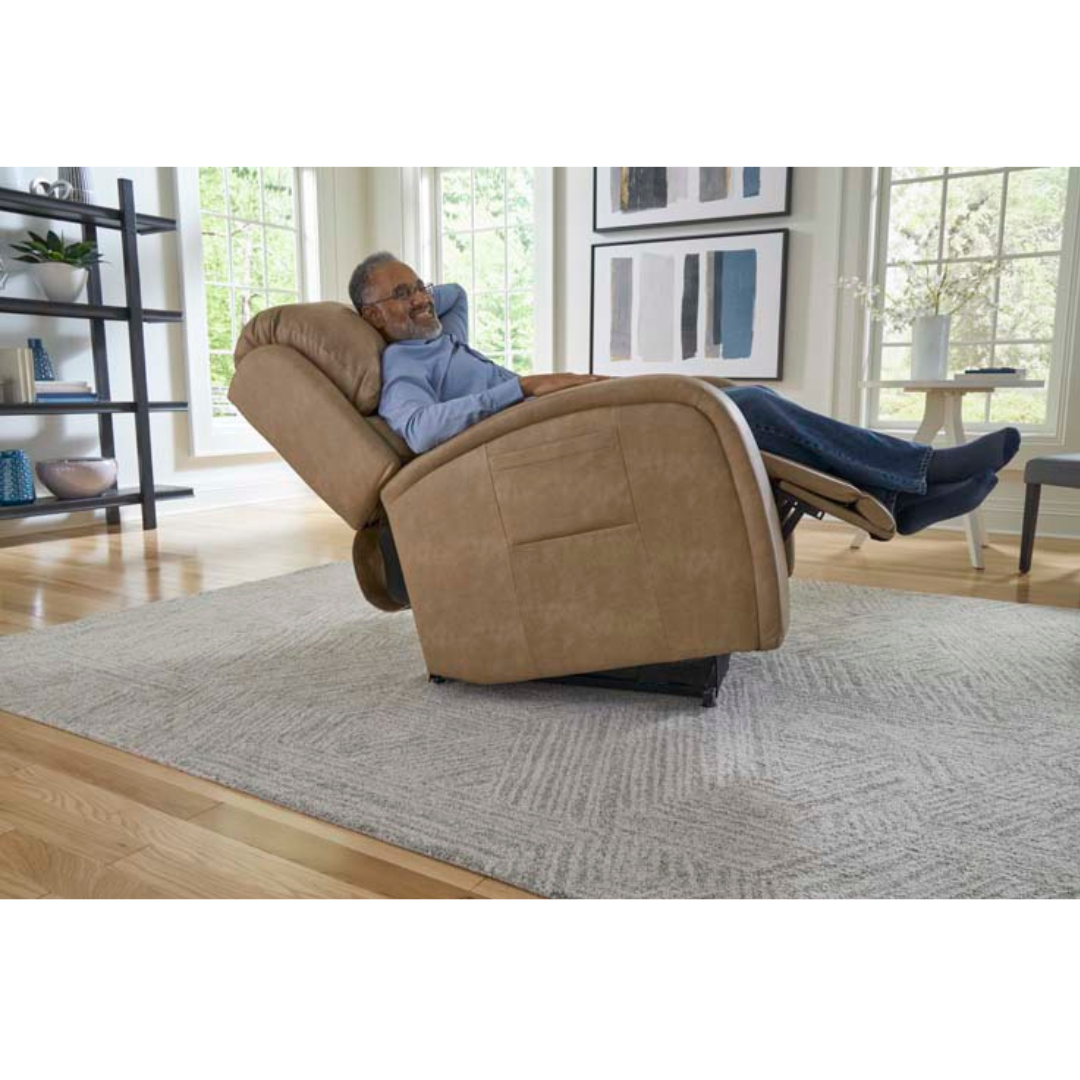 In a sunlit room adorned with large windows, abstract art, a decorated shelf, and a light rug on wooden floors, someone lounges in the Golden Tech PR761 EZ Sleeper Recliner with Lift Assist & Twilight Recline. Feet up, they enjoy the chairs 5-Zone Comfort System amidst natural light.