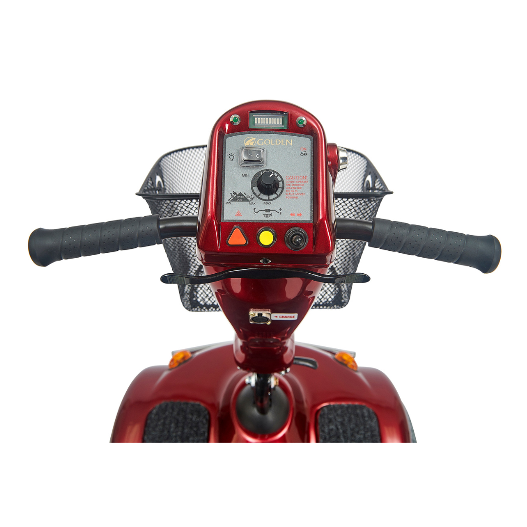 Close-up of the Golden Tech Avenger HD Bariatric Mobility Scooters handlebar and control panel. The red scooter has buttons, switches, a digital display, and a wire basket for rugged terrain. Black grips on the handlebars provide comfort for long journeys.
