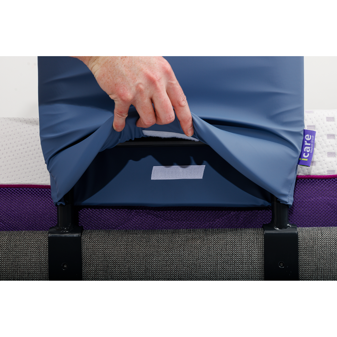 A hand lifts a blue cover to reveal an icare tag on the mattress, showing purple, white, and gray inner layers—highlighting the iCare Medical Bed Safety Rails for fall prevention and added bedside support.