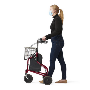 A woman in a black top and jeans, face mask on, uses a red Medline 3-Wheel Steel Rollator with all-terrain wheels and a basket. She is in profile, facing left against a plain white background.