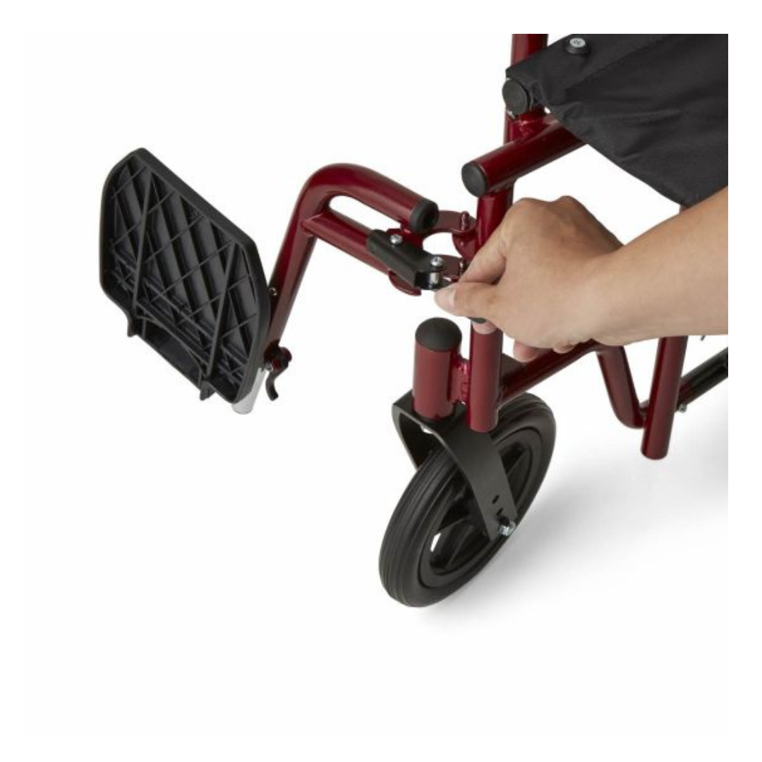 A hand adjusts the removable footrest of a red Medline Bariatric Transport Chair, showcasing its comfortable seating and durable aluminum frame. The close-up image highlights the black footrest and part of the wheel, emphasizing its lightweight design.