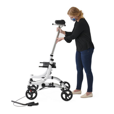 A user in a mask adjusts the height of a Medline Upright Aluminum Rollator, featuring ergonomic handbrakes, white frame with black accents, four wheels, and an upright handlebar design for stability and comfort. An adjustment tool lies nearby.