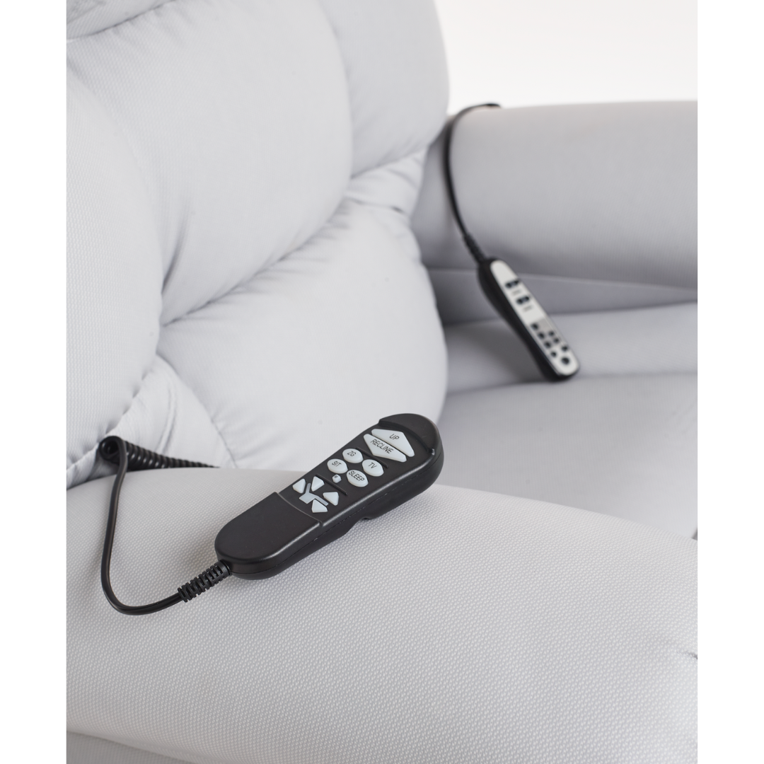 Two remote controls on a light gray cushioned armchair—a Journey Perfect Sleep Reclining Lift Chair with Heat—rest, suggesting control over features like therapeutic heat and massage. One sits on the armrest, the other on the seat. Designed for ultimate comfort.
