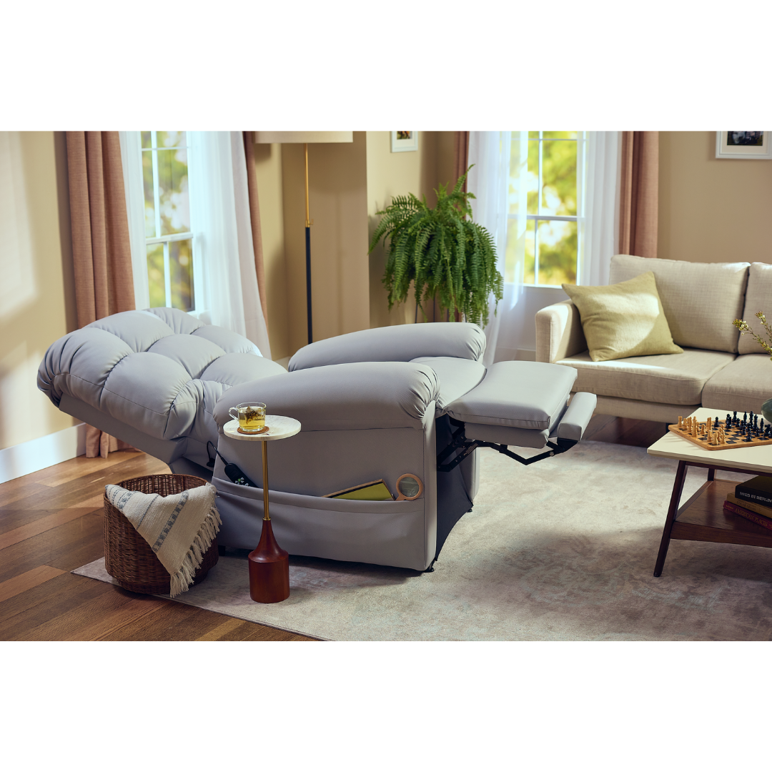 A cozy living room features the Journey Perfect Sleep Reclining Lift Chair with Heat for ultimate comfort, a small side table holding a drink, a basket with a blanket, and nearby plant. A chessboard sits on the coffee table as sunlight filters through the windows.