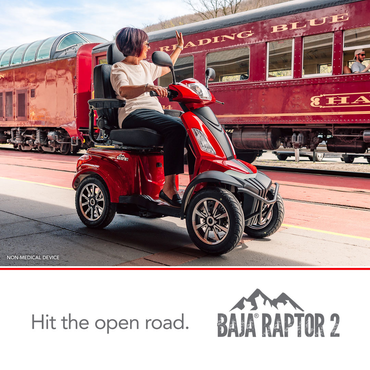 A woman enjoys premium comfort on a red Pride Baja® Raptor® 2 Bariatric 4-Wheel Scooter at a train station, gazing at a vintage red train labeled READING BLUE. Text below reads: Hit the open road. BAJA RAPTOR 2.