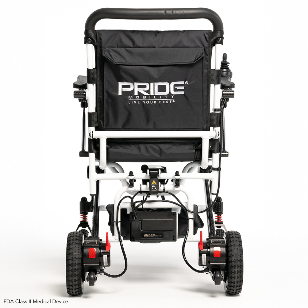Rear view of the folded Pride Mobility Jazzy® Carbon Ultralite Powerchair with a black seat cover featuring Live Your Best text. It has a lightweight frame with black and white elements, red-accented rear wheels, an airline-compliant lithium battery, and a removable joystick with USB charger.