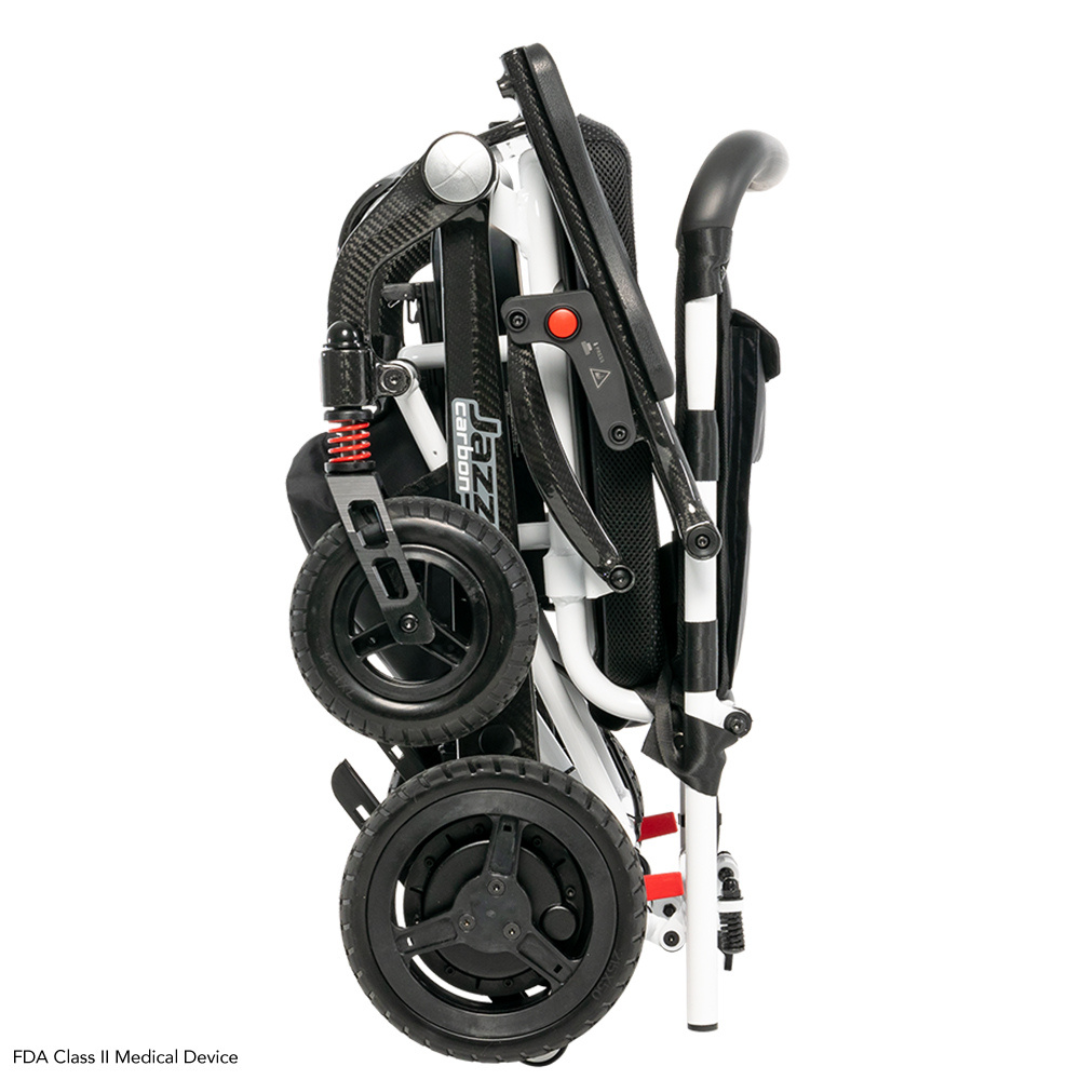 The Pride Mobility Jazzy® Carbon Ultralite Powerchair is a folded black and white scooter with small wheels and visible springs. Its ultra-lightweight, compact, and features ergonomic handles for easy transport. It includes a removable joystick with USB charger.