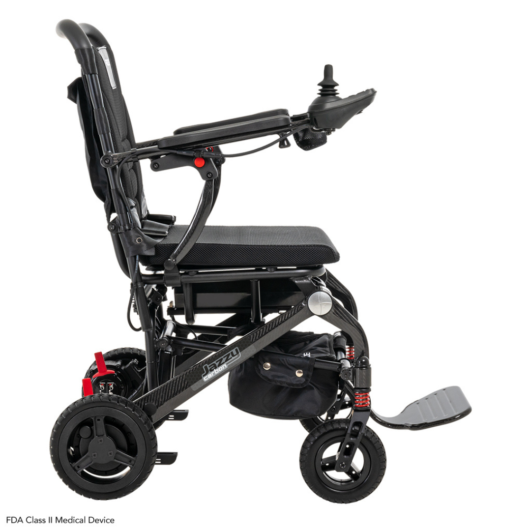 Introducing the Pride Mobility Jazzy® Carbon Ultralite Powerchair, a sleek black electric wheelchair with joystick control on the right armrest, a foldable footrest, four wheels, and striking red accents for superior mobility assistance during your adventures.