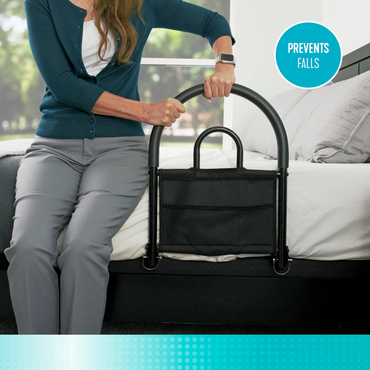 A woman grips the Stander Bed Rail Advantage Traveler, a portable safety rail for traditional beds. A circular label on the image reads “PREVENTS FALLS.”.