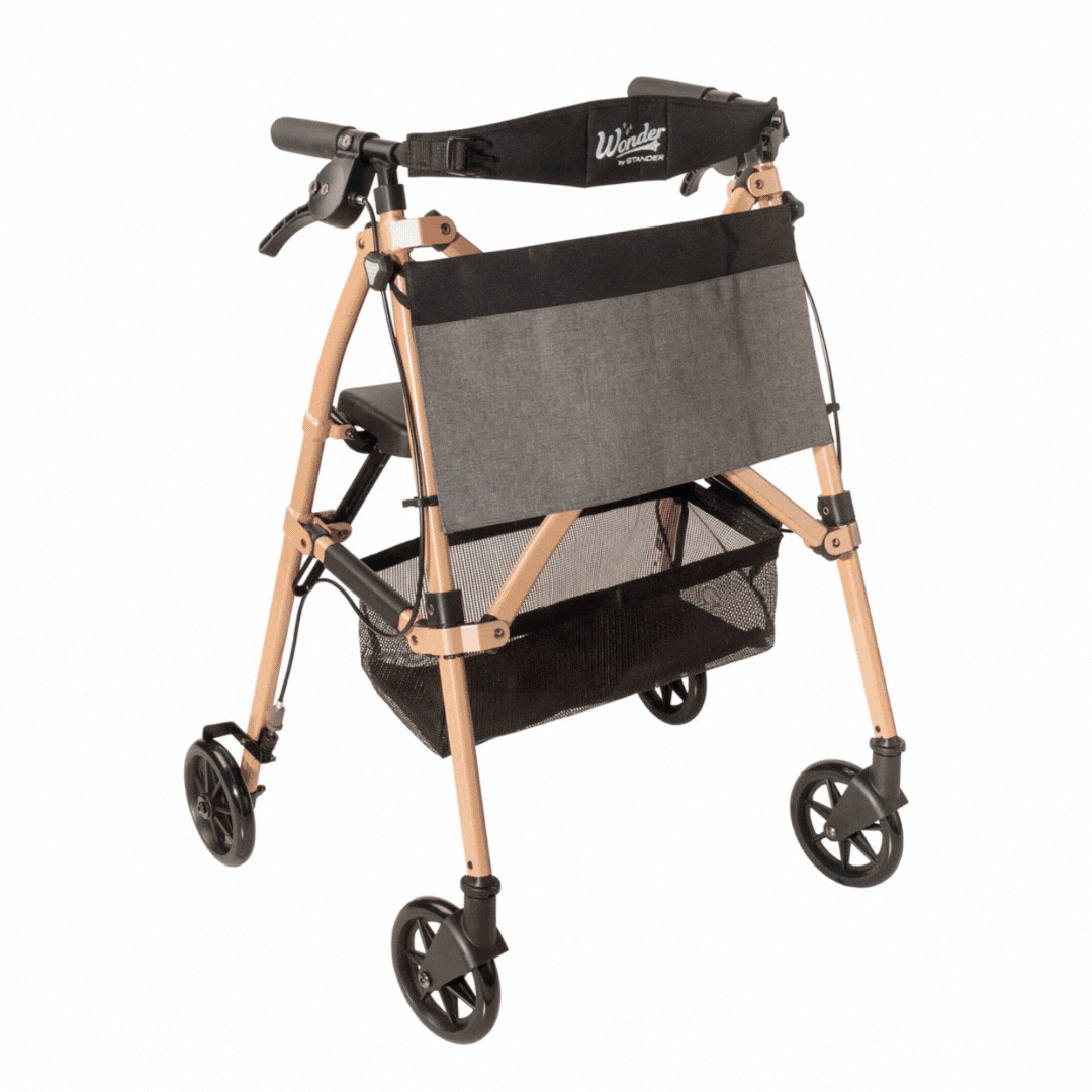 The Stander Wonder Rollator Plus is a lightweight, compact four-wheel rollator with a tan frame, black accents, grey fabric seat, storage basket, and hand brakes—ideal for travel and daily mobility assistance.