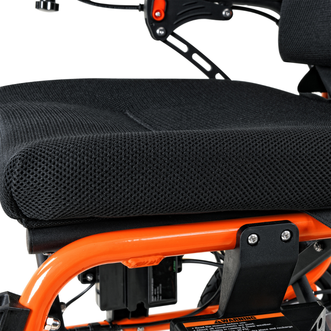 Close-up of a black cushioned seat on the SuperHandy GoRide 2, an orange-framed electric wheelchair weighing only 40 lbs. It features visible bolts and supports, with a textured non-slip seating area and parts of its mechanical components partially visible beneath.