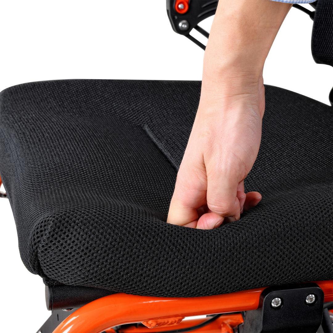 A person pressing down on the soft cushioned seat of a SuperHandy GoRide 2 Portable Electric Wheelchair with a lightweight ergonomic design, demonstrating its flexibility and comfort. The focus is on the hand and the seat.