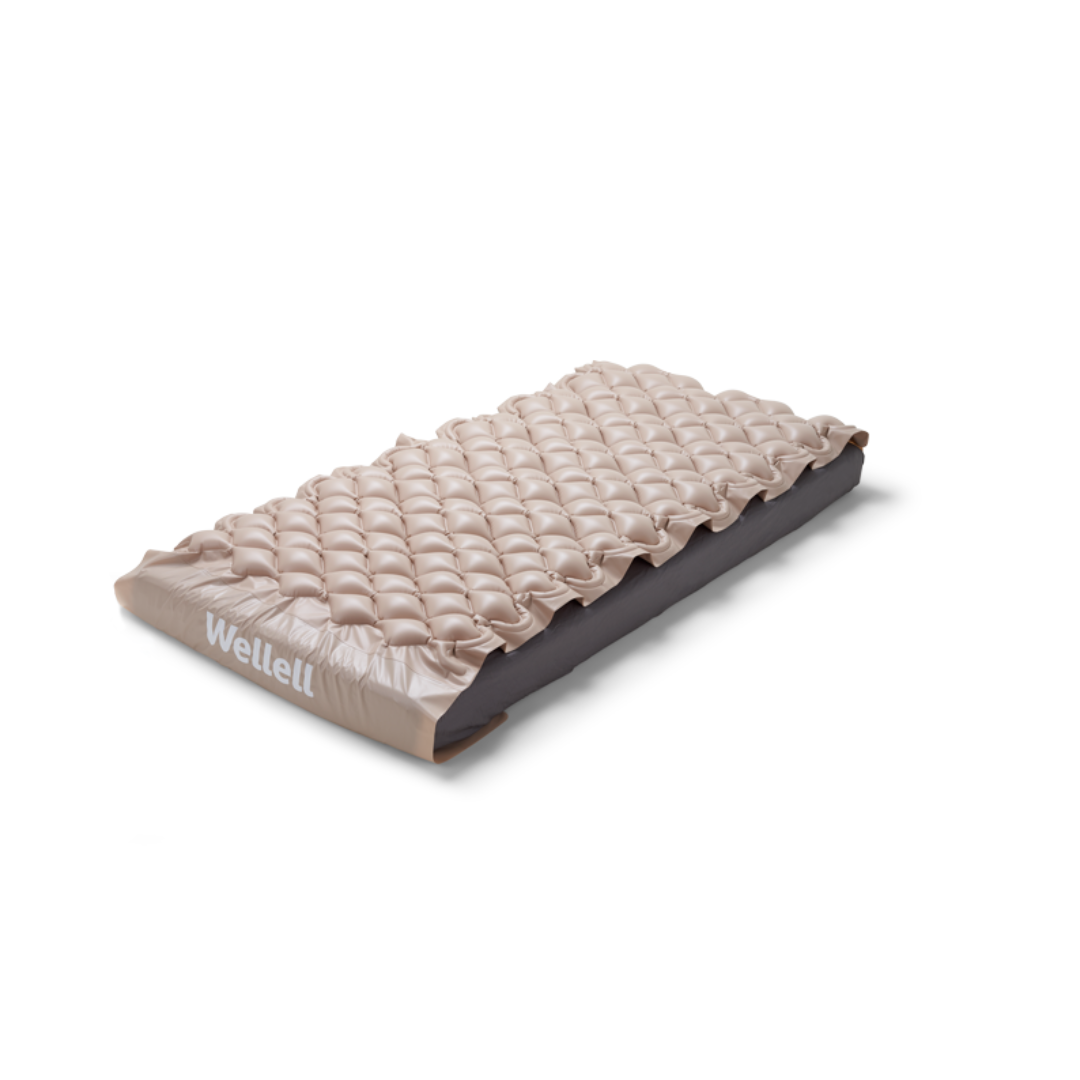 The Wellell Domus 1 Alternating Pressure Mattress is an inflatable, light brown mattress with a bubble surface, designed for pressure ulcer prevention and placed on a flat surface.