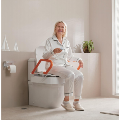 An older woman in pajamas smiles while sitting on a toilet equipped with bright orange grab bars in a well-lit bathroom. She holds the remote for her EasyRise Powered Toilet Seat Lifter | VOCIC AX12 Pro, and there’s a plant along with sailboat decorations on the nearby shelf.