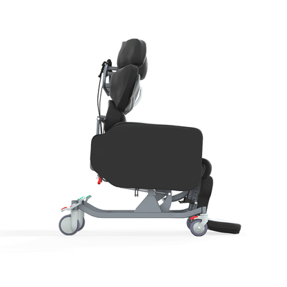 Side view of the Accora Configura® Advance Postural Tilt Chair in black with padded head, back, and leg support. The ergonomic chair has a metal frame, wheels, footrests, adjustment levers, and a modern design for advanced postural care.