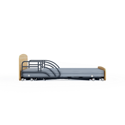The Accora Contesa® FloorBed® Hi/Low Full Electric Bed is a modern hospital bed with a light wood headboard/footboard, metal safety rails, and wheels—a smart fall-prevention solution, shown from the side against a white background.
