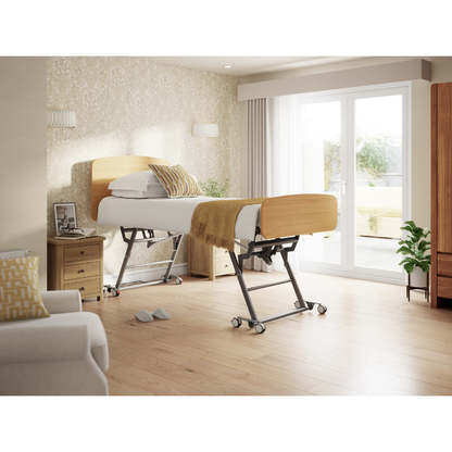A modern bedroom with an Accora Contesa® FloorBed® Hi/Low Full Electric Bed—adjustable for fall prevention—adorned with a yellow blanket and pillow, plus a bedside table, armchair, lush plants, and large windows with sheer curtains.
