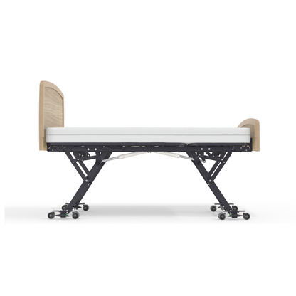 The Accora Empresa® Full Electric Bariatric FloorBed® is shown from the side, featuring a white mattress, wooden headboard and footboard, and a black adjustable metal frame on wheels against a white background.