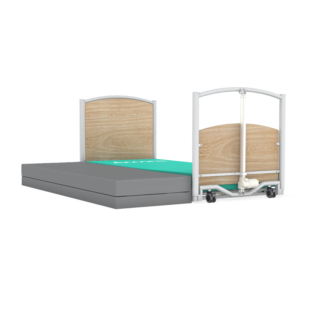 The Accora FloorBed® Ultra Low Full Electric Homecare Bed features a light wood headboard and footboard, a green surface area with grey mattress sections, is low to the ground, and has wheels visible on the footboard.
