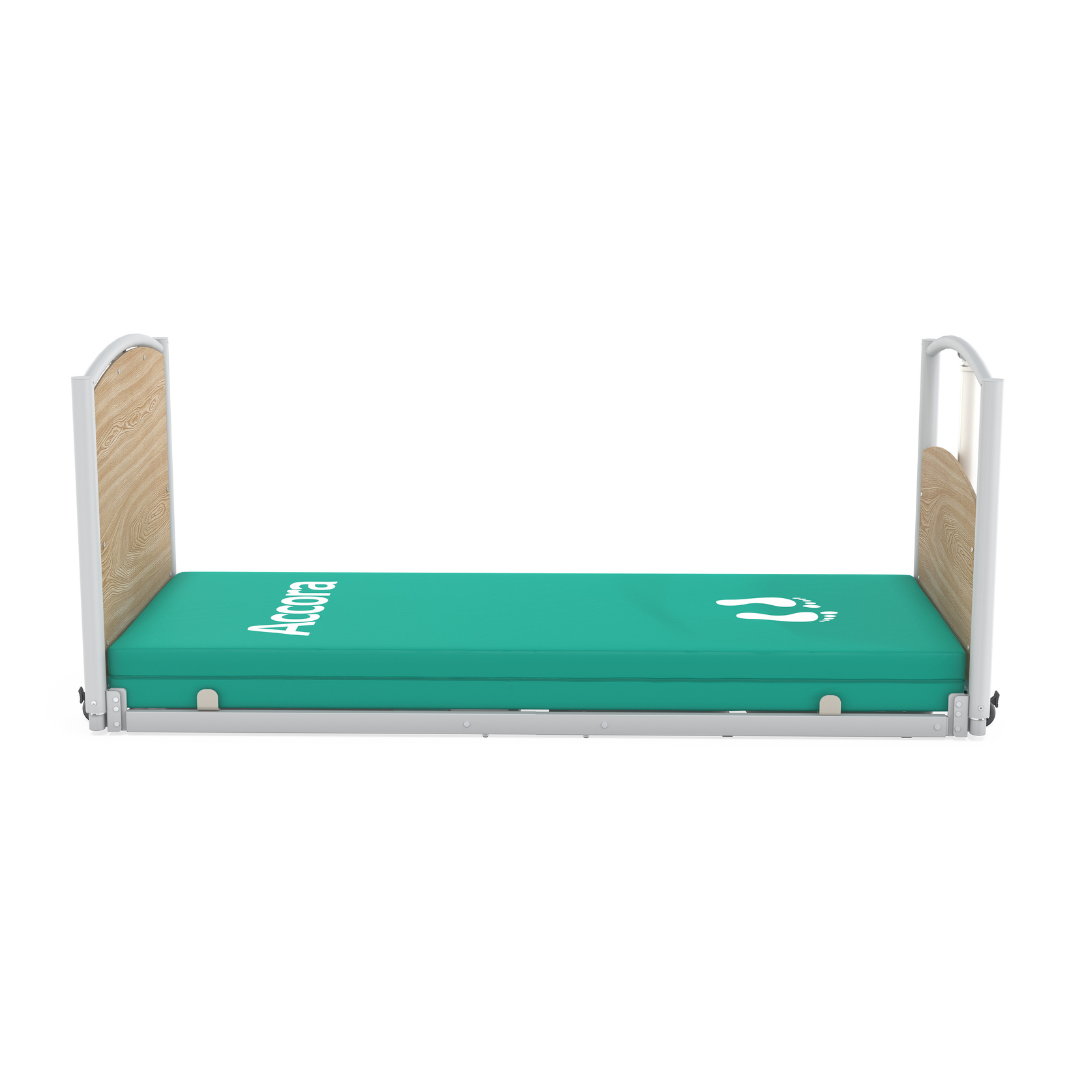 The Accora FloorBed® Ultra Low Full Electric Homecare Bed features wooden headboards and a green Accora-labeled mattress with a white footprint graphic, offering enhanced safety and comfort.