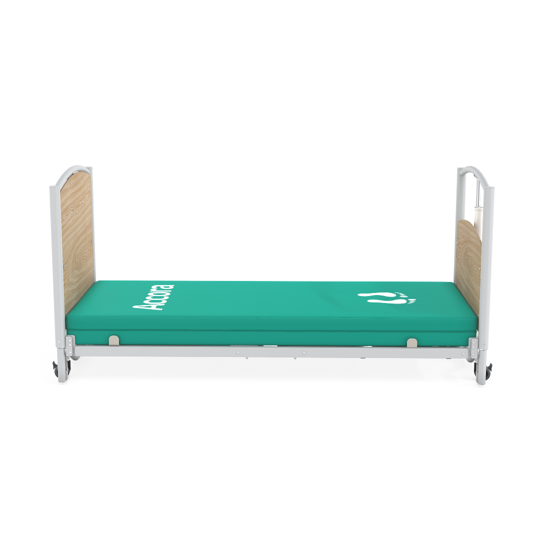 A hospital bed with side rails, light wood headboard and footboard, and a green mattress with white medical symbols and "Antica," styled as an Accora FloorBed® Ultra Low Full Electric Homecare Bed.