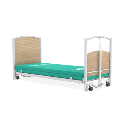 The Accora FloorBed® Ultra Low Full Electric Homecare Bed is shown from the side with a light wood headboard and footboard, green mattress, and white metal frame on wheels, offering enhanced safety and comfort in care settings.