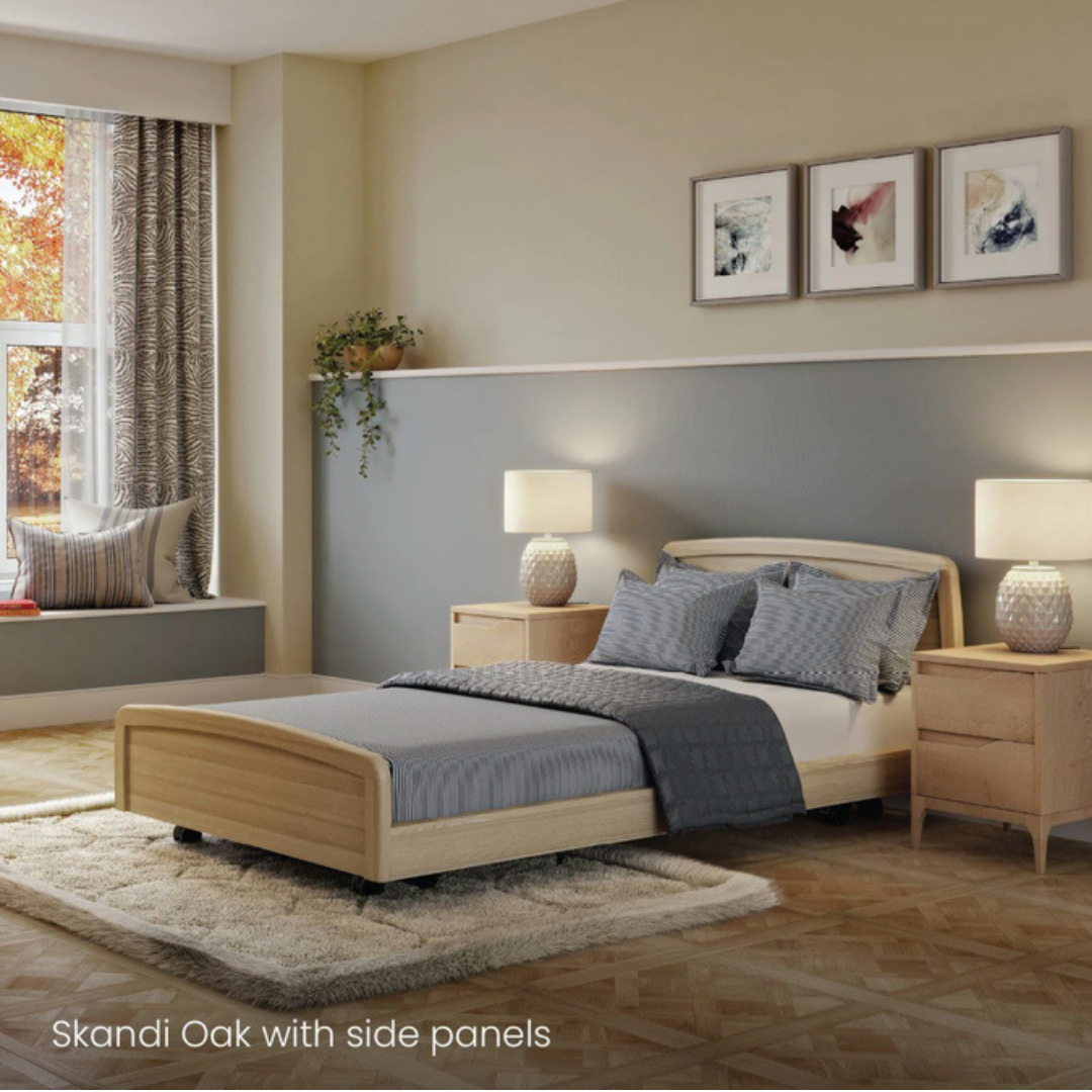 A modern bedroom features the Accora Contesa® FloorBed® Hi/Low Full Electric Bed in Skandi Oak with side panels, blue-gray bedding, matching lamps on bedside tables, a large curtained window, wall art, and light wood floors.
