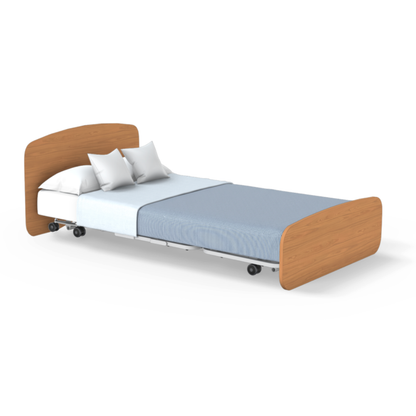 The Accora Empresa® Full Electric Bariatric FloorBed® features a light wood headboard and footboard, sturdy metal frame, wheels, white pillows and sheet, plus a light blue blanket—ideal for modern care facility layouts.