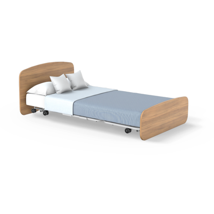 The Accora Empresa® Full Electric Bariatric FloorBed® features a wooden headboard and footboard, a white mattress, light blue blanket, and two white pillows. The bed is on wheels against a plain white background.