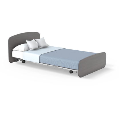 The Accora Empresa® Full Electric Bariatric FloorBed® is shown with wheels, a light blue sheet, two white pillows, and light brown headboard and footboard, all displayed on a white background for clear viewing.