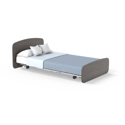 The Accora Empresa® Full Electric Bariatric FloorBed® features a dark wooden headboard and footboard, white mattress, two white pillows, light blue bedding, and wheels—perfect for versatile bedroom styling on a white background.