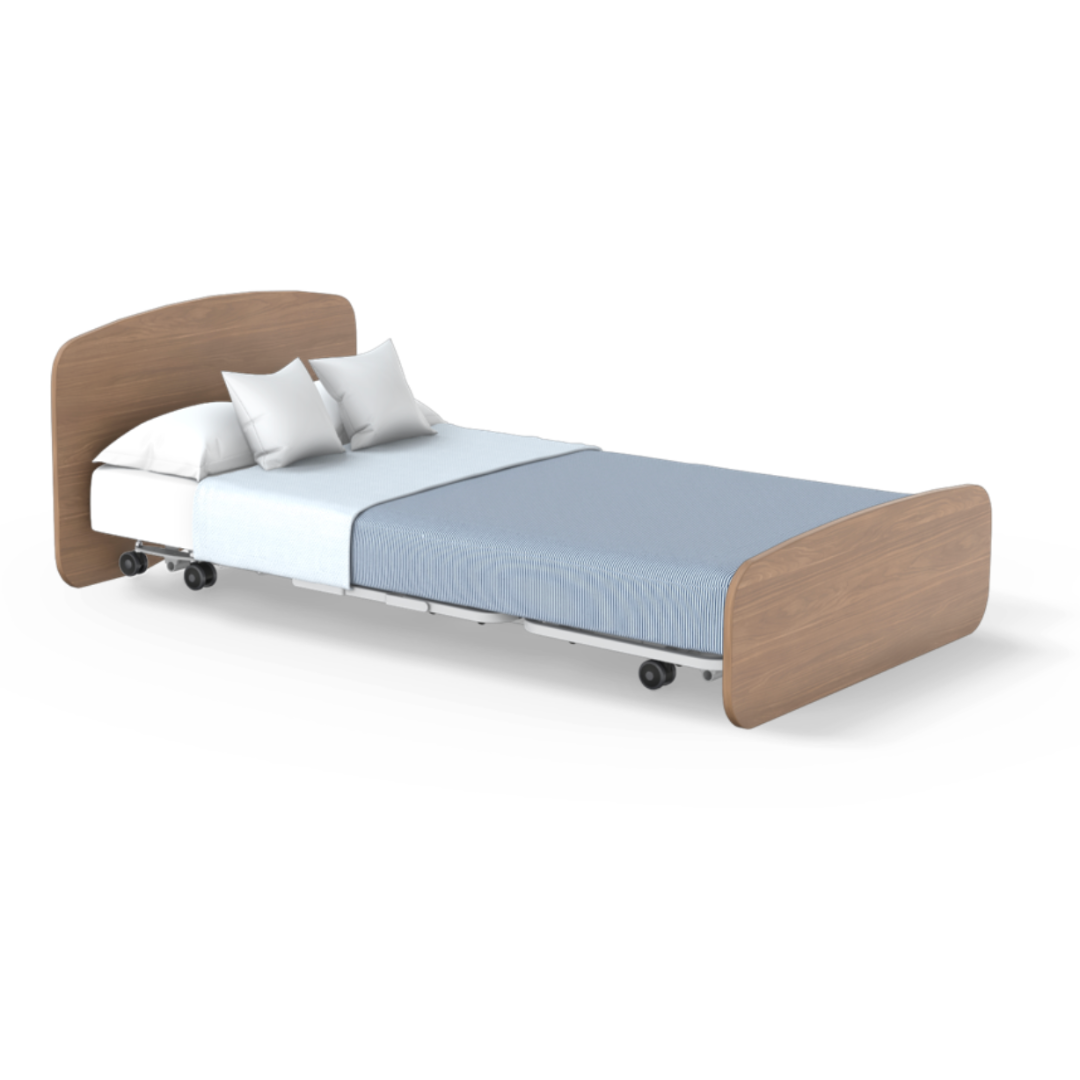 The Accora Empresa® Full Electric Bariatric FloorBed® is shown with a light wood headboard and footboard, white mattress, blue blanket, two white pillows, and caster wheels—ideal for healthcare environments.