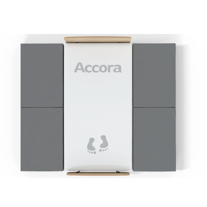 Overhead view of the High Safety Mat For Bedside Falls: a white rectangular Accora platform with gray padding on both sides, wooden bars at each end, and illustrated footprints near the bottom for high-impact fall protection.