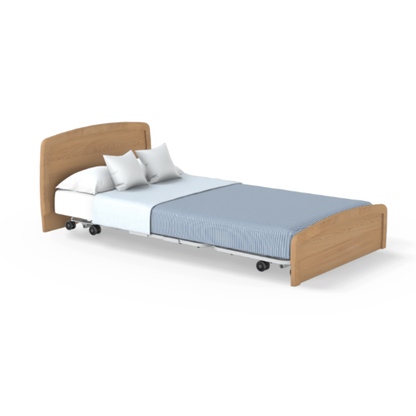 The Accora Empresa® Full Electric Bariatric FloorBed® features a light wood headboard and footboard, white sheets, two white pillows, and a light blue blanket. It is on wheels and displayed against a white background.