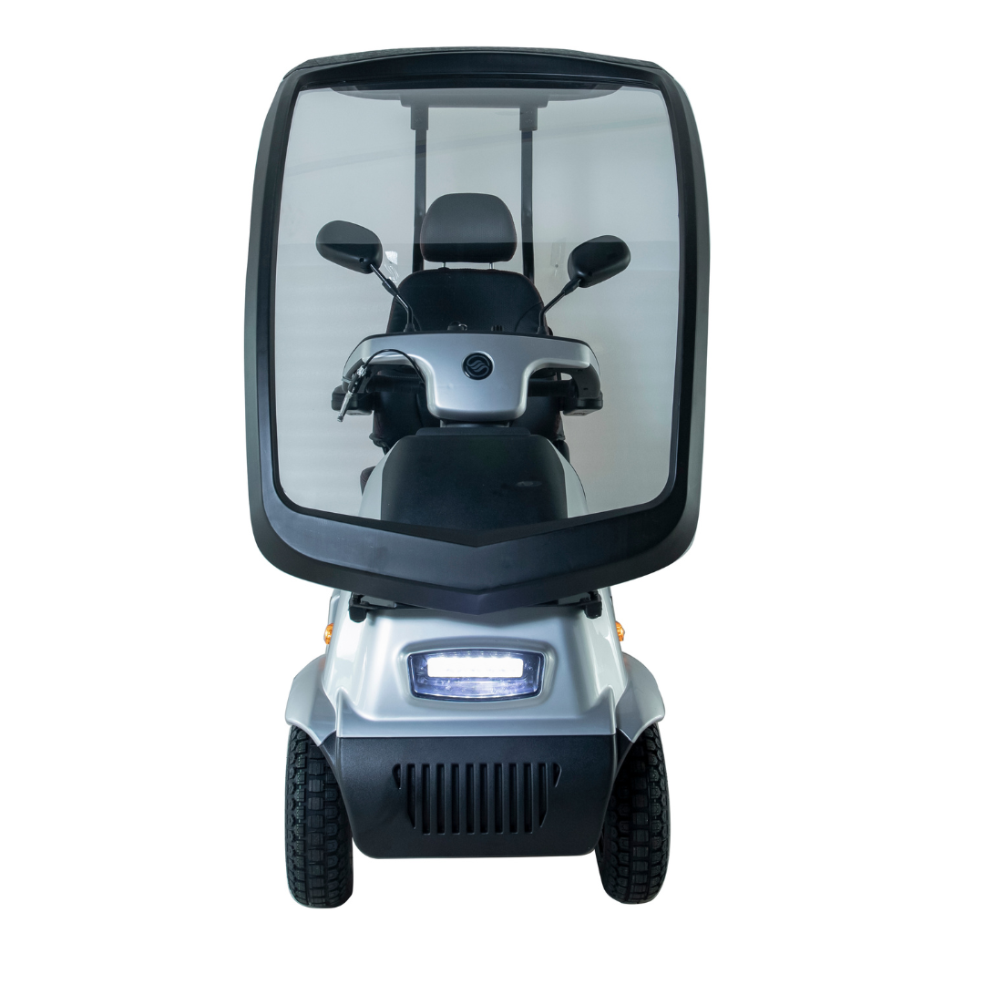 Front view of the silver Afikim Afiscooter C4 HD 4-Wheel Mobility Scooter featuring a transparent windshield and enclosed cabin, four wheels, headlight, rearview mirrors, and an orthopedic seat for comfort and weather protection.