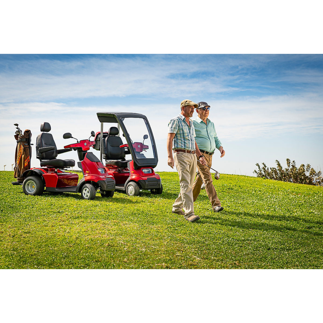 Two individuals in casual wear and caps walk on a grassy hill under a blue sky. Nearby, an Afikim Afiscooter Solar, featuring solar charging efficiency and a canopy-covered windshield, is parked with golf clubs visible at the back.