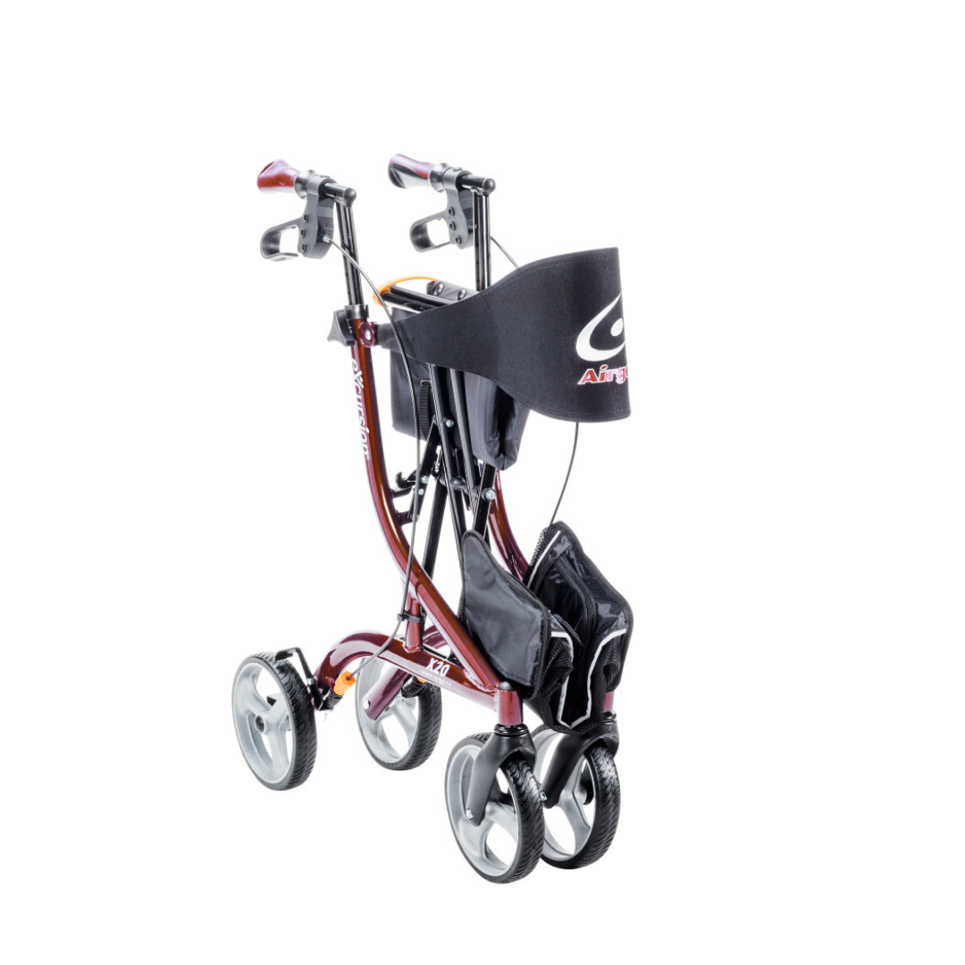 The Drive Airgo eXcursion X20 Lightweight Side-fold Rollator is shown folded for portability; it features a red frame, four wheels, black handles and seat, plus a storage pouch.