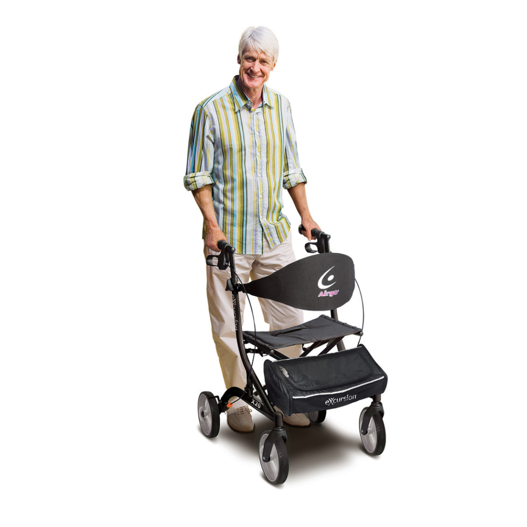 A smiling older adult with gray hair stands behind a Drive Airgo eXcursion X20 Lightweight Side-fold Rollator with a seat, bag, and Airgo logo, against a white background.