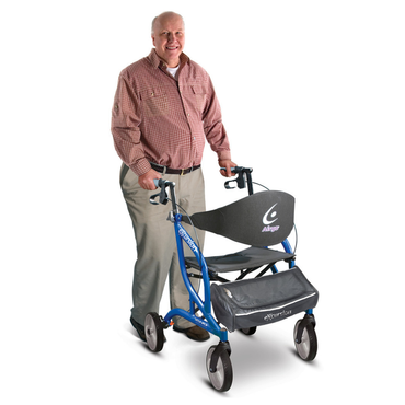 A smiling older man in a red plaid shirt and khaki pants stands behind a Drive Airgo eXcursion XWD Lightweight Bariatric Rollator, which features a black seat and storage pouch.
