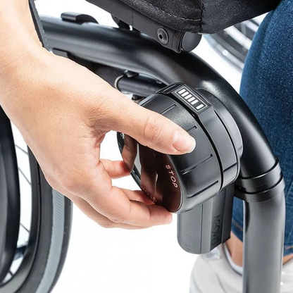 Close-up of a hand adjusting a control knob on a wheelchair equipped with the Alber SMOOV One Power Assist. The knob’s display shows several bars and the word STOP.